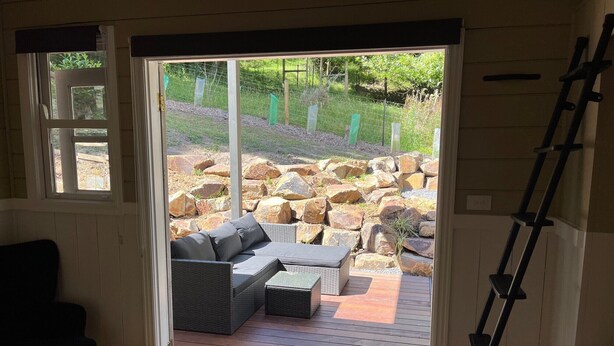 Een kamer met een schuifdeur naar een terras buiten met een bank en een houten terras.