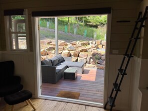 A room with a sliding glass door leading to an outdoor patio with a sofa and a wooden deck. - Ferntree Digs Cottage (Warburton)