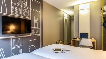 Een hotelkamer met een bed, een tv aan de muur, een bureau met een laptop, een stoel en een spiegel.
