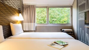 A hotel room with a bed, a window with a view of trees, a lamp, and a wall with a chalkboard design. - Ibis Jouy en Josas Velizy (Jouy-en-Josas)