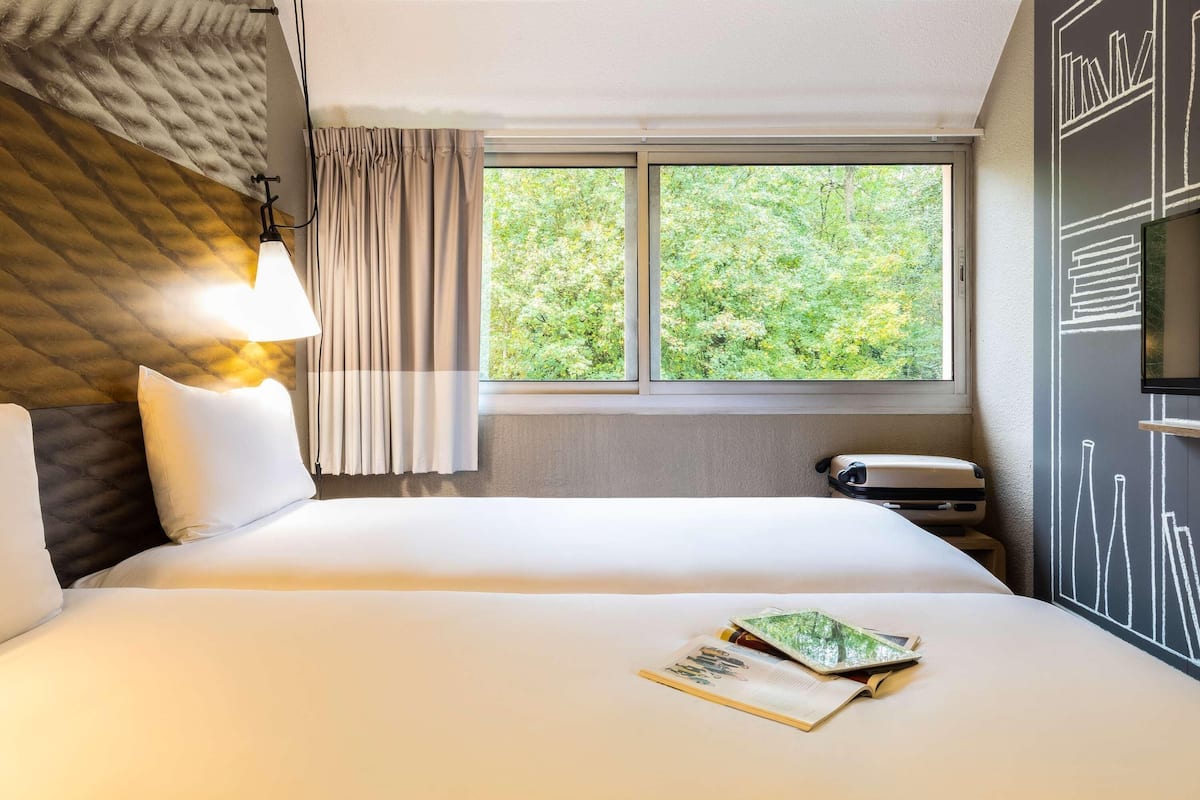 Ein Hotelzimmer mit Bett, Fenster mit Blick auf Bäume, einer Lampe und einer Wand mit Kreidetafel-Design.