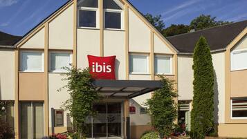 A hotel with a prominent 'ibis' sign, a covered entrance, and potted plants in front.
