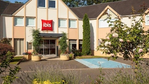 A hotel with a prominent red ibis sign, a swimming pool, and a landscaped garden. - Ibis Jouy en Josas Velizy (Jouy-en-Josas)