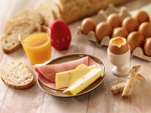 A breakfast setting with bread, eggs, cheese, and juice. - Ibis Jouy en Josas Velizy (Jouy-en-Josas)