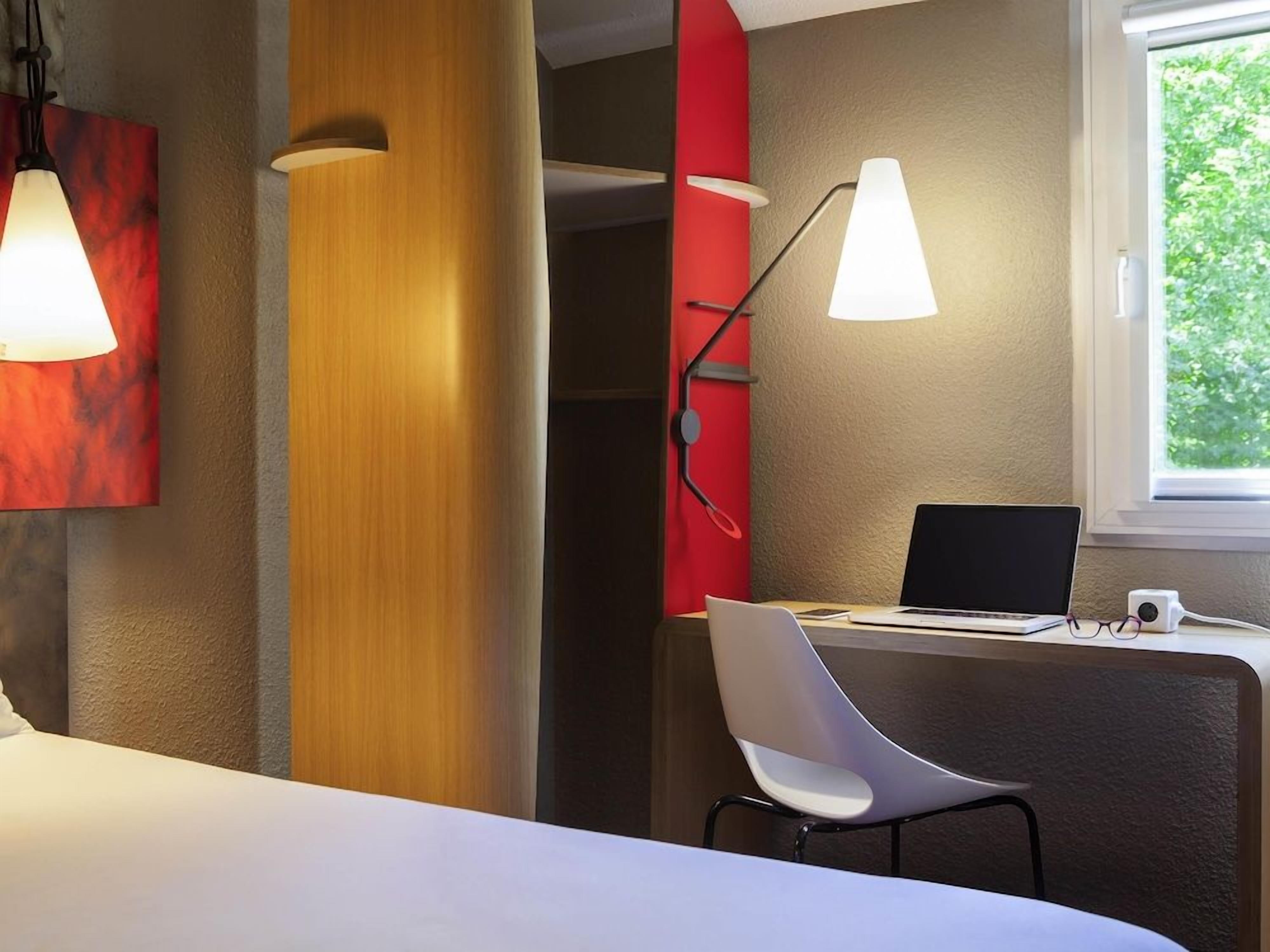 Une chambre d’hôtel avec un lit, un bureau avec un ordinateur portable, une chaise et deux lampes fixées au mur.