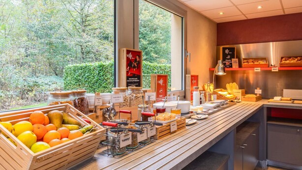 A buffet area with a variety of food items, a fruit display, and a view of the outdoors. - Ibis Jouy en Josas Velizy (Jouy-en-Josas)