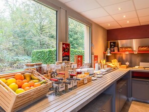 A buffet area with a variety of food items, a fruit display, and a view of the outdoors. - Ibis Jouy en Josas Velizy (Jouy-en-Josas)
