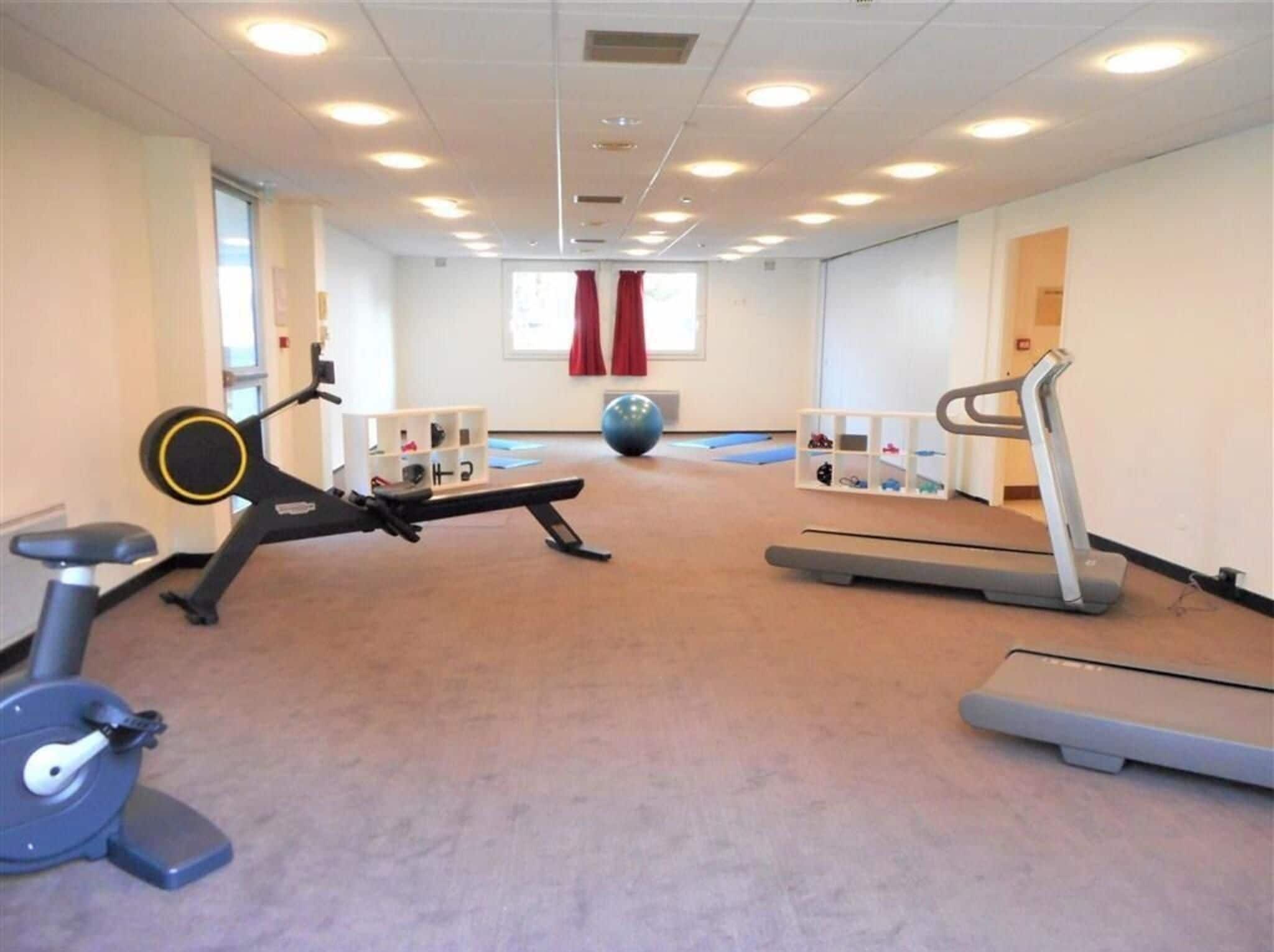 A fitness room with exercise equipment, a large exercise ball, and a window with red curtains.