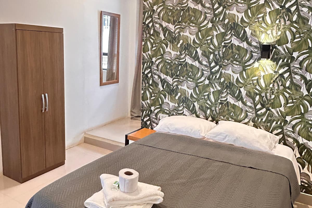 Una habitación de hotel con una cama, un armario, un espejo y una pared con un diseño de hojas.