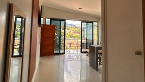 Un intérieur spacieux avec une grande porte-fenêtre coulissante donnant sur un patio extérieur, un mur recouvert de panneaux en bois et un sol carrelé.
