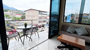Un salon moderne doté d’une grande porte-fenêtre coulissante donnant sur un balcon. La pièce comprend un canapé, une table basse en bois et une table à manger avec des chaises.