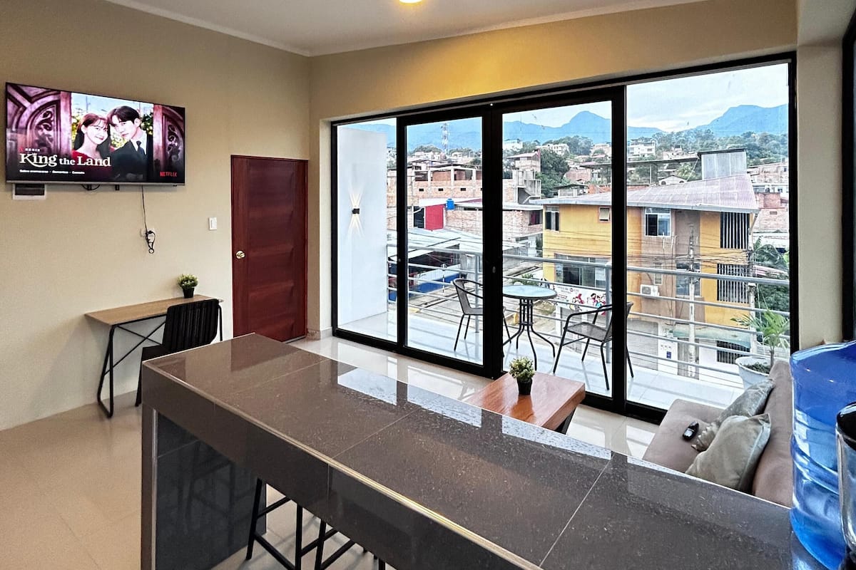 Una cocina moderna con una isla grande, un comedor con sillas y un ventanal con vista a la ciudad.