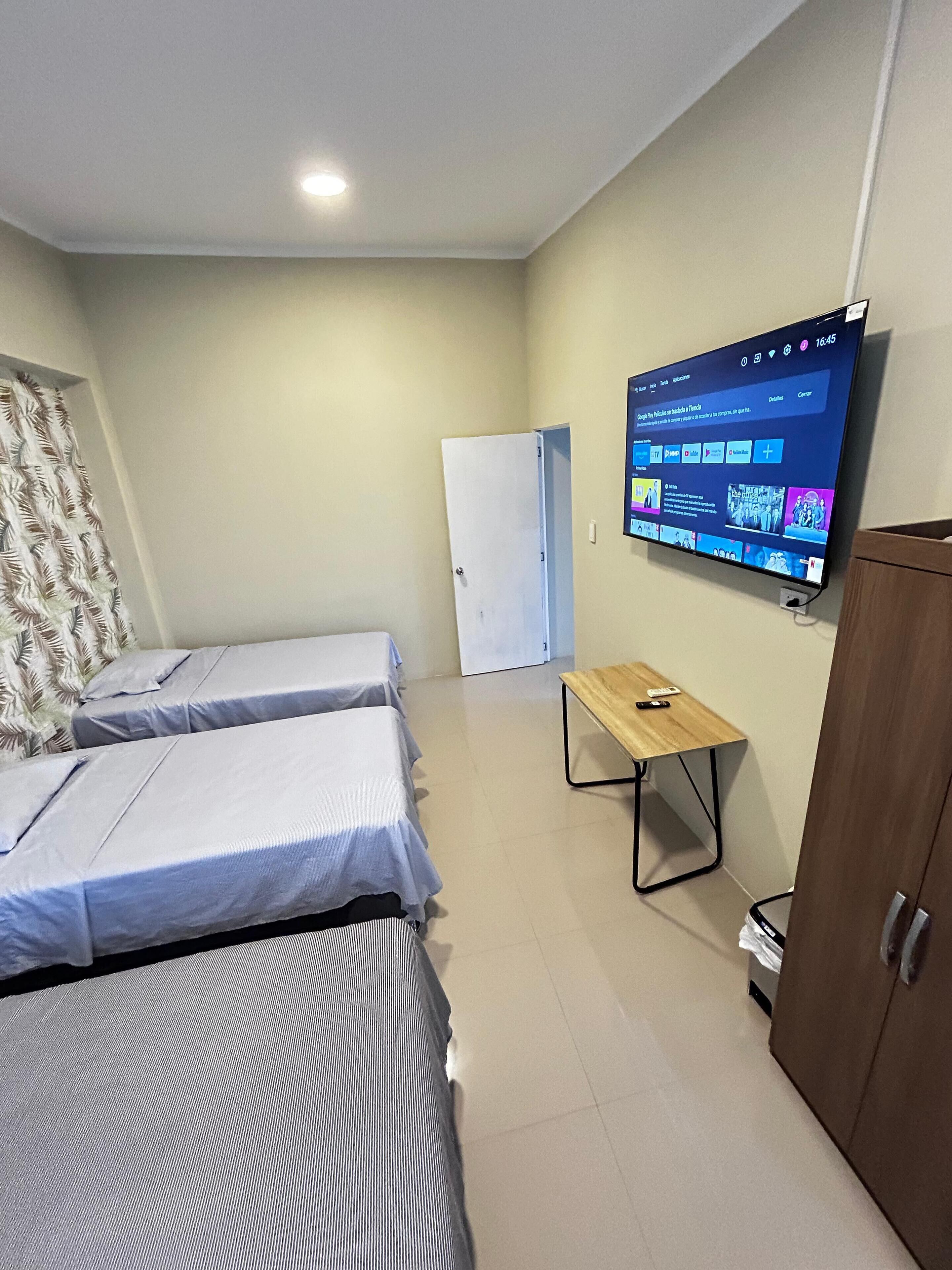 A room with two beds, a television mounted on the wall, a wooden table, and a door.