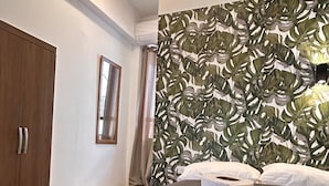 Une chambre d’hôtel avec un lit, une armoire en bois, un miroir et un mur orné d’un motif végétal.