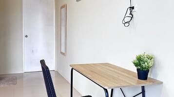 Una habitación con televisión montada en la pared, una mesa con una planta en maceta, una silla y una puerta.
