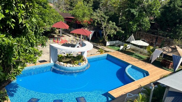 Une piscine avec trois chaises longues, entourée de verdure et agrémentée d’une petite structure circulaire surmontée d’un toit.