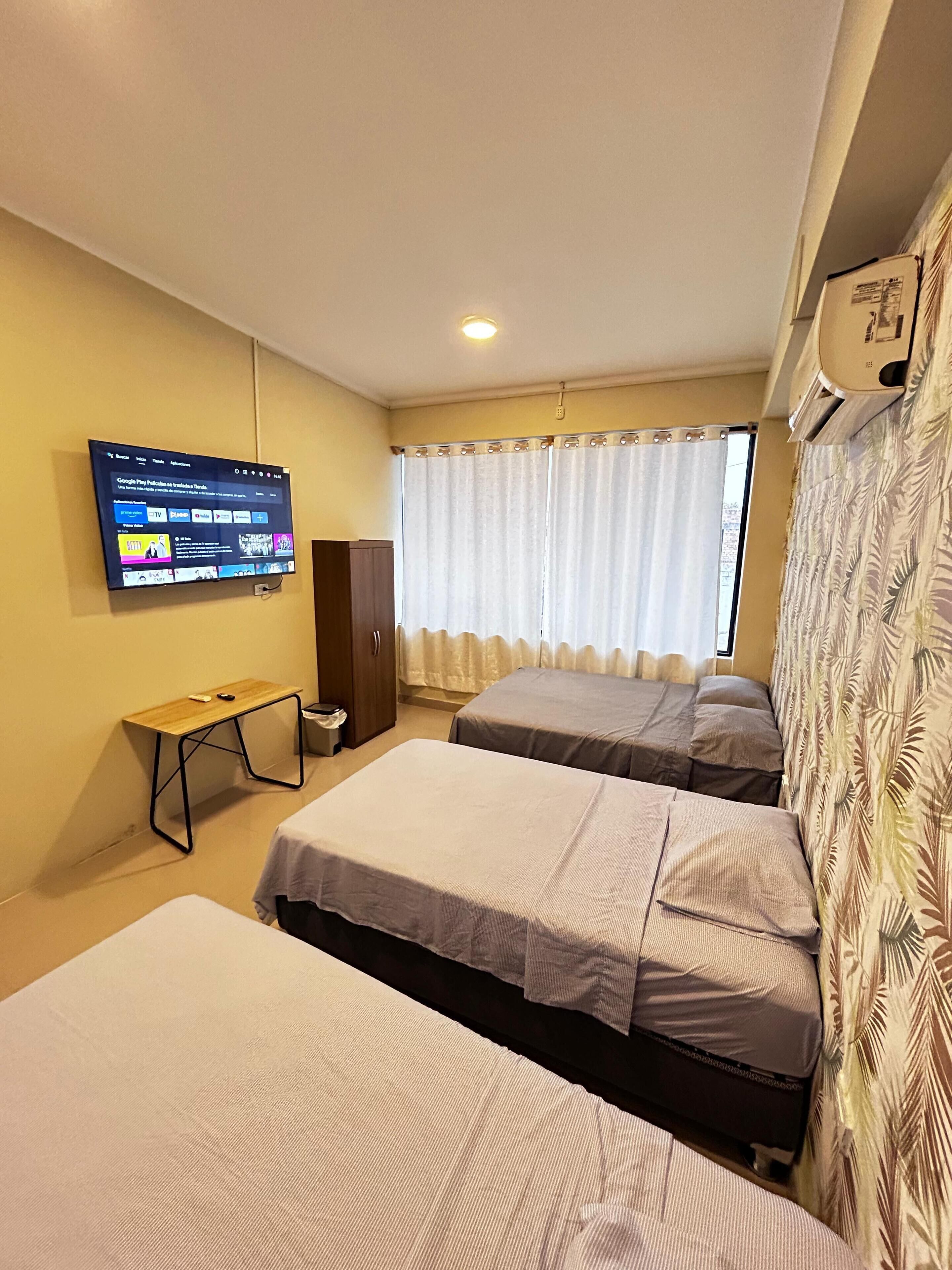Habitación de hotel con dos camas, un televisor en la pared, un escritorio y un armario.