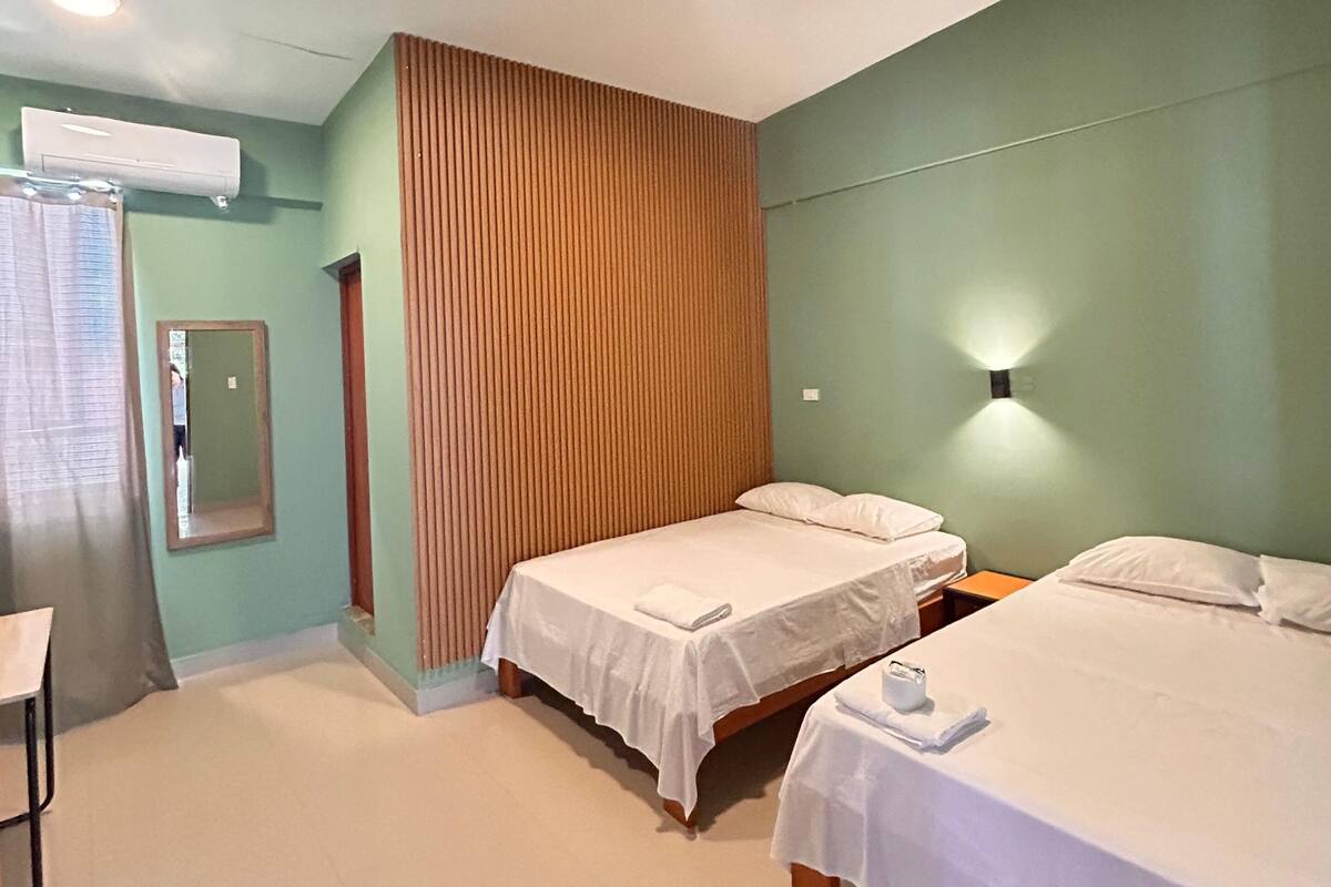 Habitación de hotel con dos camas, un espejo, aire acondicionado y una cortina.