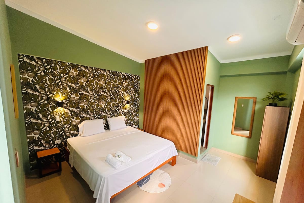Una habitación de hotel con una cama, cabecero de madera, un espejo y pared verde.