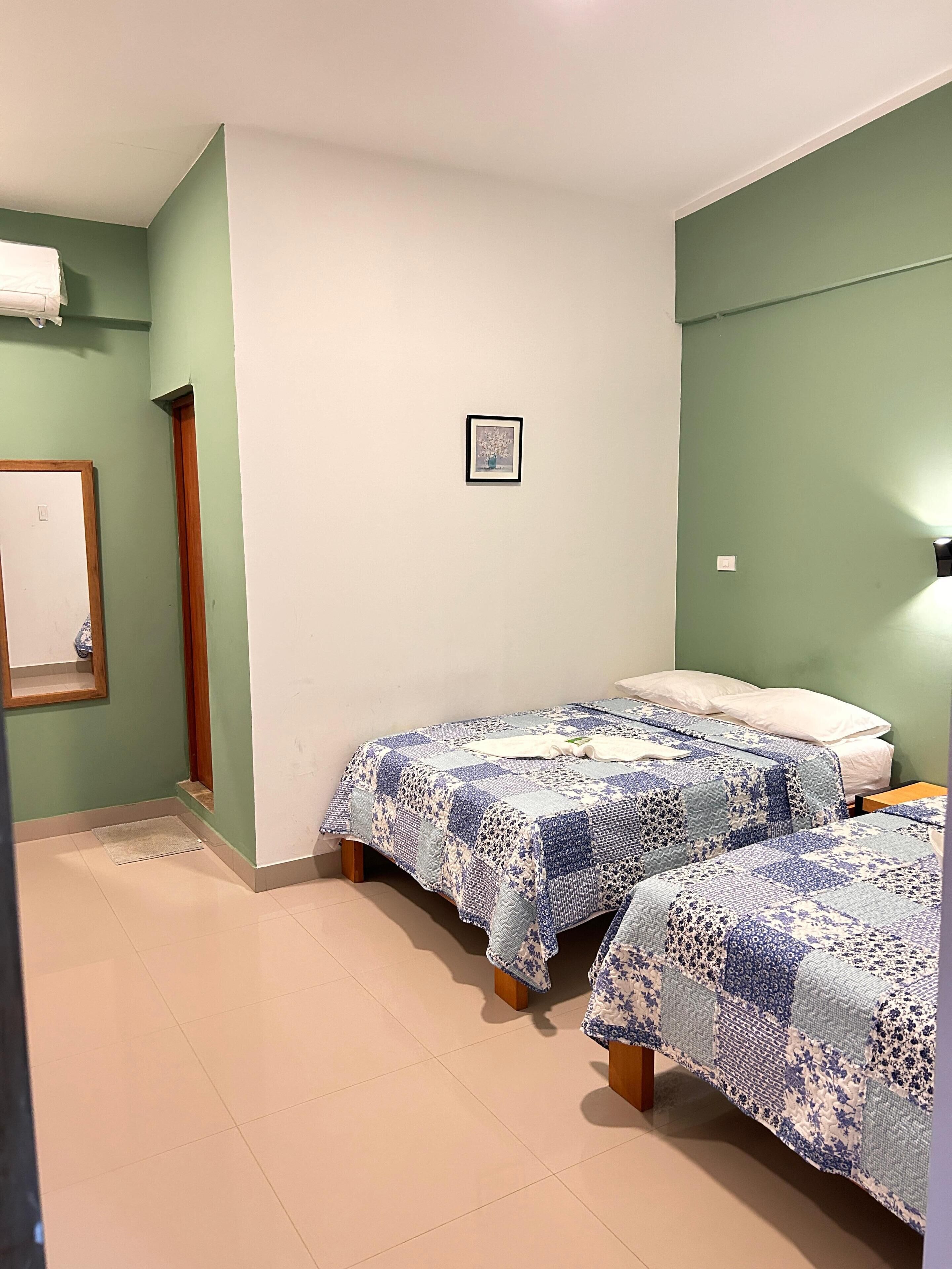 A room with two beds, a framed picture on the wall, and a door with a mirror.