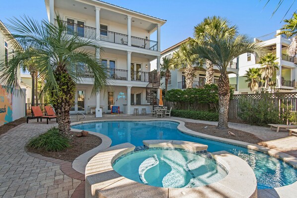 Zona de piscina con jacuzzi, palmeras y mobiliario exterior.