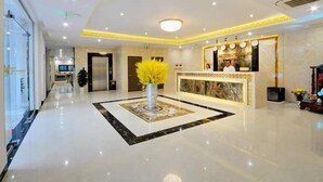 A hotel lobby with a reception desk, a large vase with yellow flowers, and a marble floor.