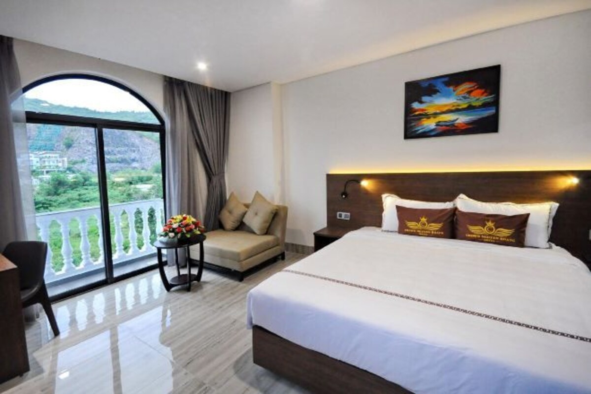 Een hotelkamer met een groot bed, een bank, een tafel met bloemen, een schilderij aan de muur en een balkon met uitzicht.