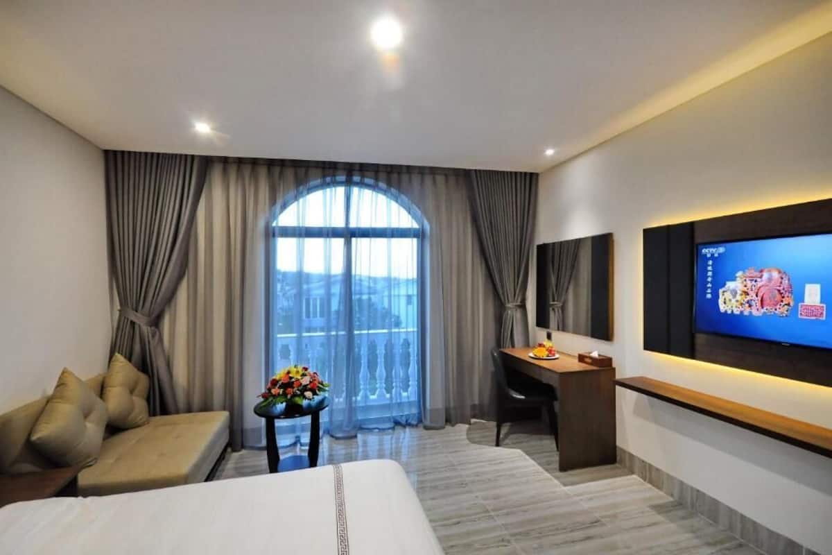 Een hotelkamer met een bed, een slaapbank, een bureau, een televisie en een groot raam met gordijnen.