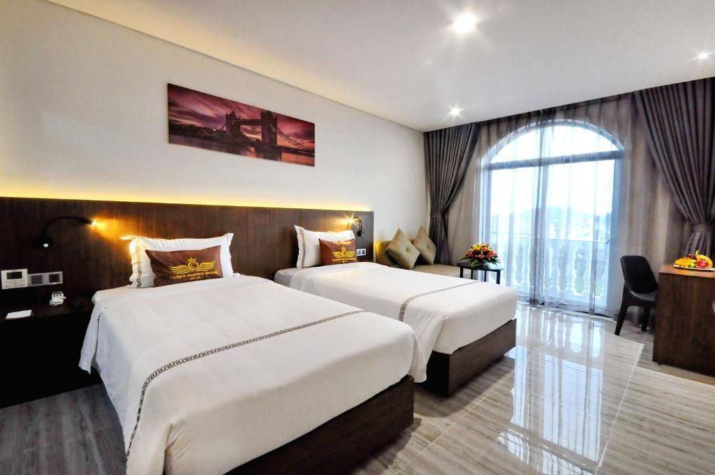 A hotel room with two beds, a desk, a chair, and a large window with curtains.