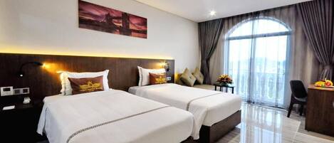 A hotel room with two beds, a desk, a chair, and a large window with curtains.