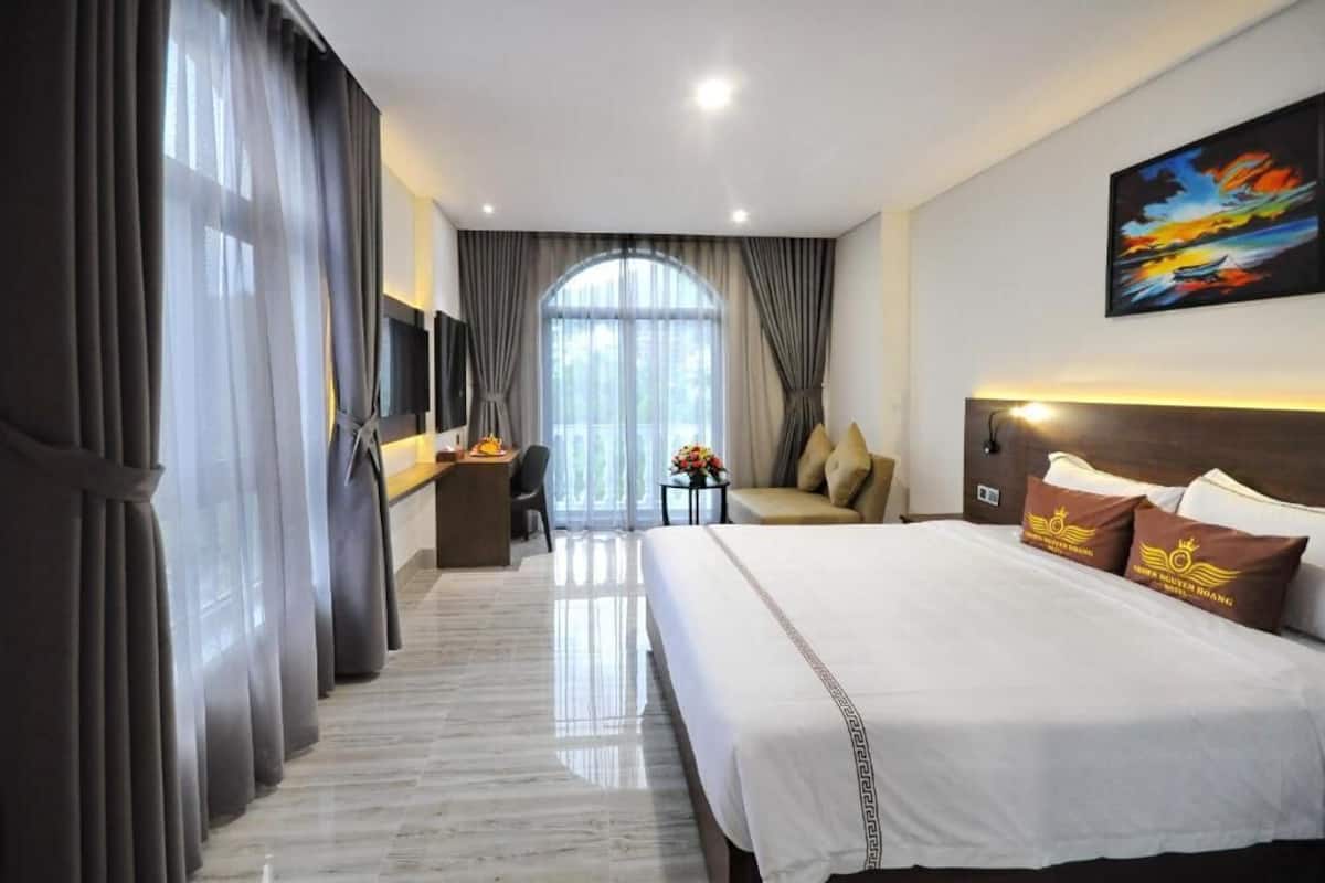 Hotelkamer met een groot bed, een bureau, een stoel en uitzicht op de omgeving door een groot raam.