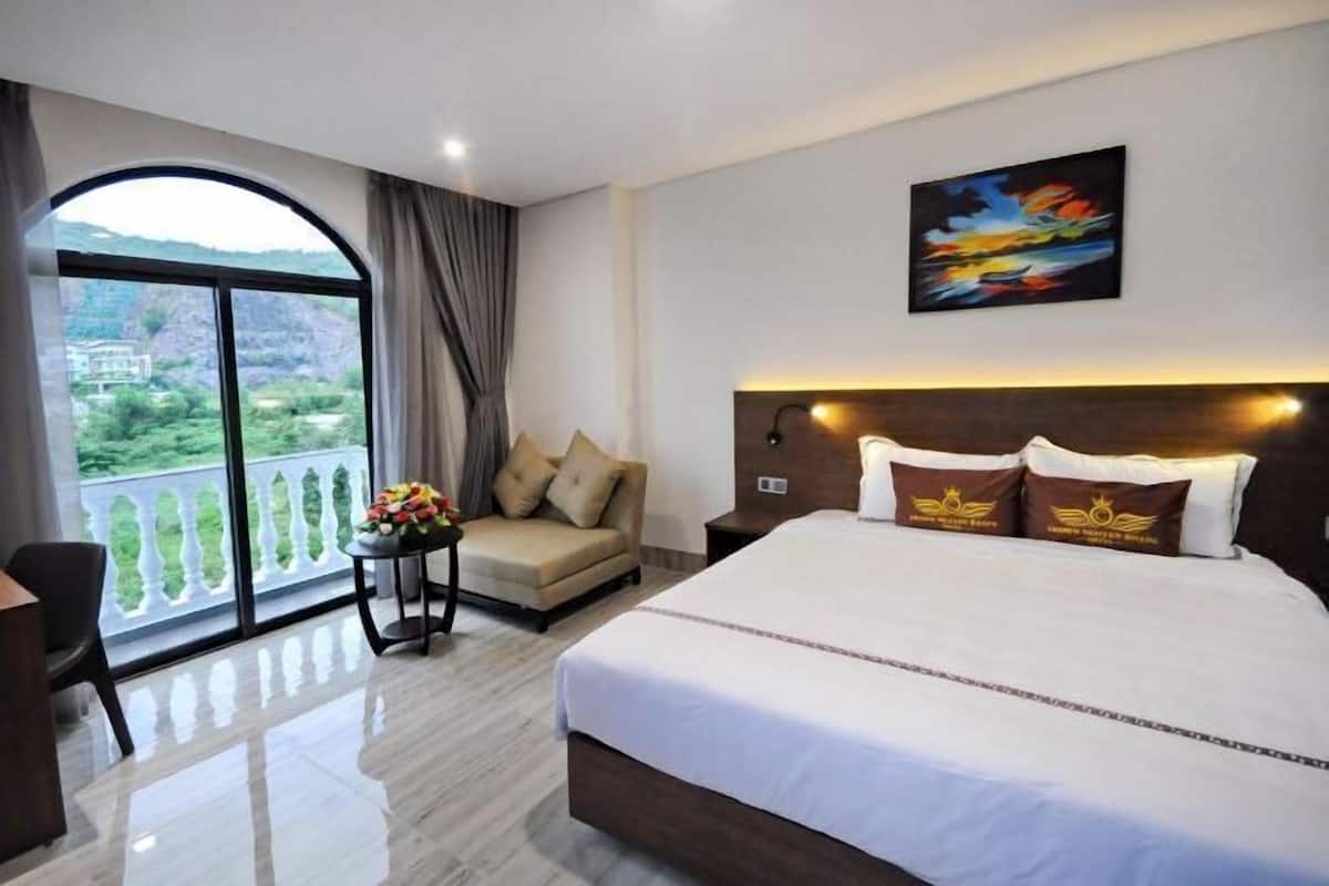 Een hotelkamer met een groot bed, een bank, een tafel met bloemen, een schilderij aan de muur en een balkon met uitzicht.