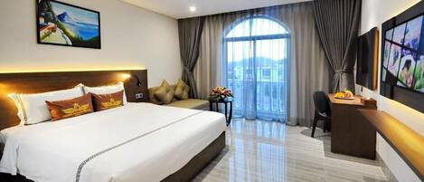 A hotel room with a large bed, a desk, a chair, and a TV.