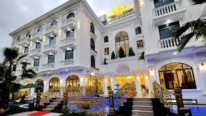 A grand hotel with multiple balconies, a central staircase, and a well-lit entrance.