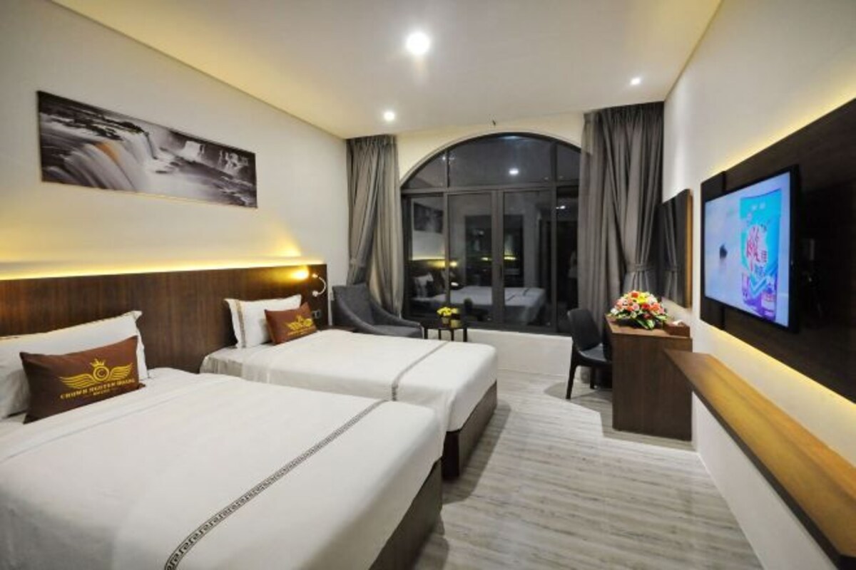Een hotelkamer met twee bedden, een bureau met televisie, een groot raam en uitzicht op buiten.