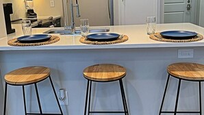 A kitchen with a central island, three stools, a microwave, and a refrigerator. - Deep Ellum Comfort Stay, Sleeps 5 - Walk to Nightlife & Dining (Dallas)