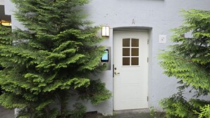 Uma porta branca com janela, cercada por árvores verdes exuberantes.