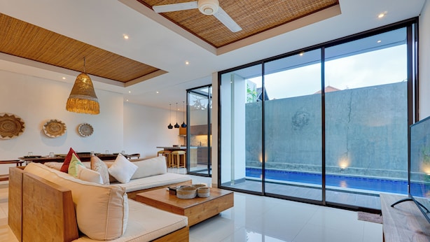 A modern living room with a large sofa, a coffee table, and a view of a swimming pool through large glass doors. - Villa Laviosa - Petitenget (Seminyak)