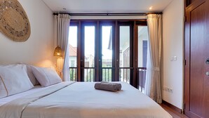 A large bed with white linens, a wooden door, and a view through a glass door to the outside. - Villa Laviosa - Petitenget (Seminyak)