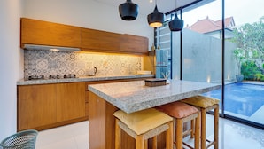 A modern kitchen with wooden cabinets, a marble countertop, and a large island with bar stools. - Villa Laviosa - Petitenget (Seminyak)