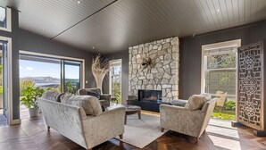 Un salon spacieux doté d’une cheminée en pierre, de sièges confortables et de grandes fenêtres offrant une vue sur l’extérieur.