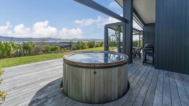 Un bain à remous sur une terrasse en bois, avec vue sur la mer et les collines.