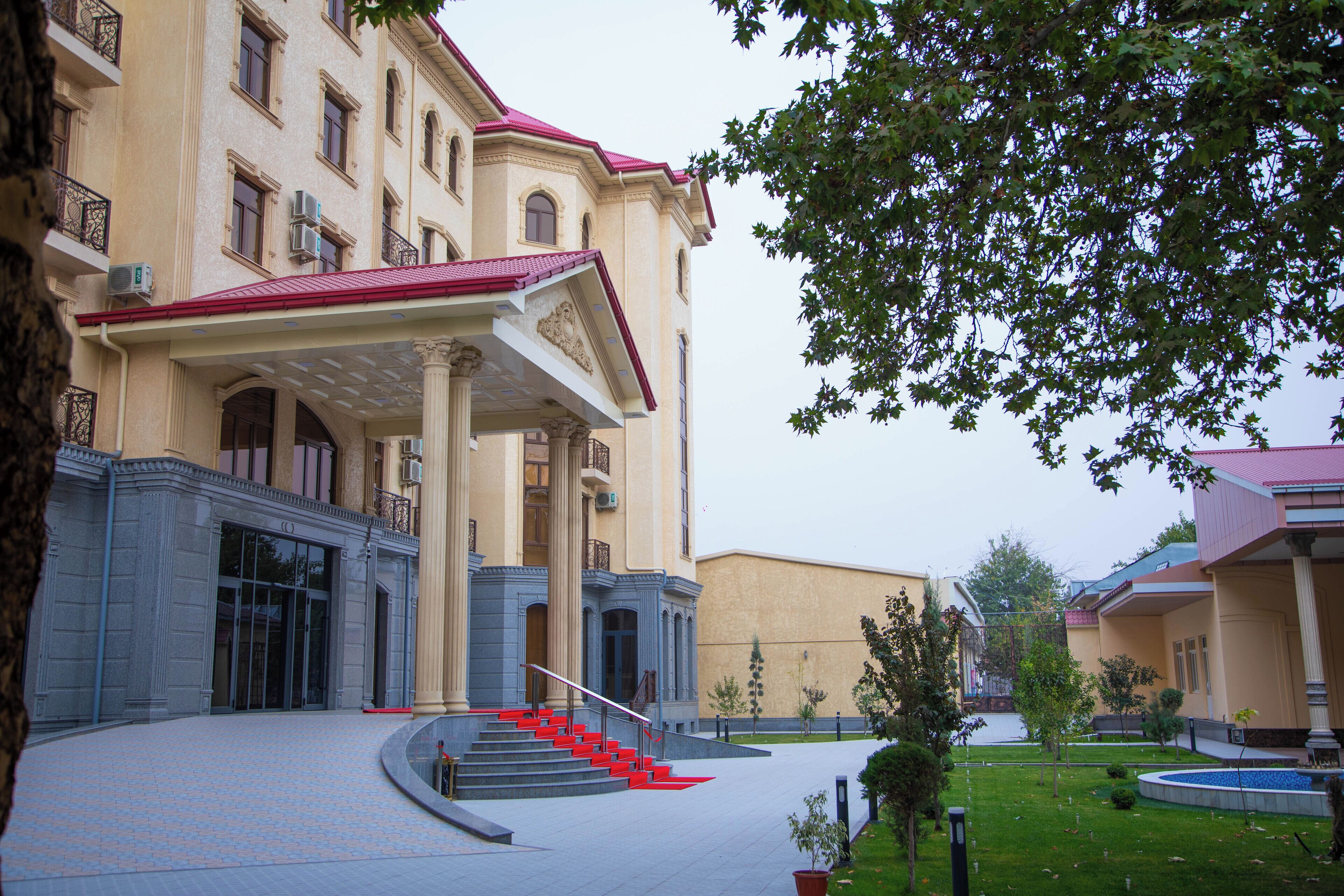 Um edifício com uma entrada imponente, uma escadaria que leva à entrada principal e uma área de gramado bem cuidada.