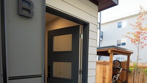 Een moderne entree van een huis met een houten poort, een deurmat en een fiets die tegen een houten constructie leunt.