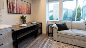 Een moderne woonkamer met een bank, een eettafel met stoelen, een groot schilderij en een raam met zonwering.