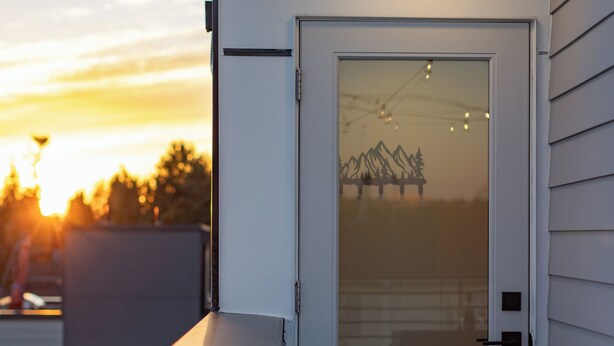 Een modern gebouw met een glazen deur, een terras en een uitzicht op bergen bij zonsondergang.