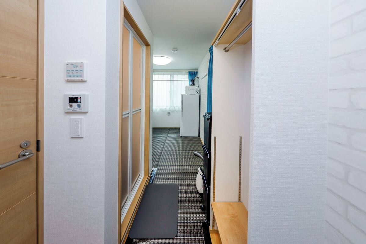 A narrow hallway with a wooden door, a thermostat, and a bench.