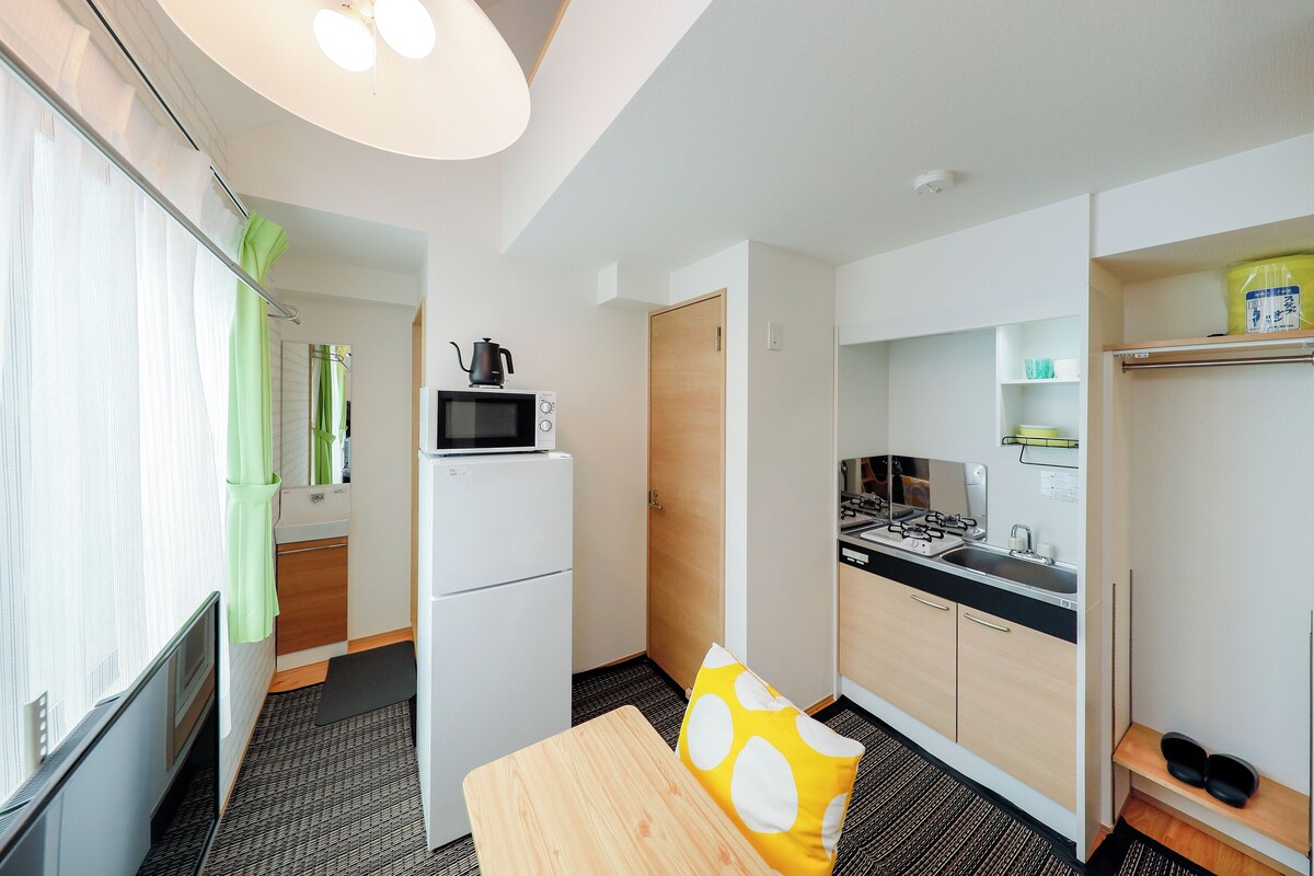 A compact hotel room with a kitchenette, a small dining area, and a shower.