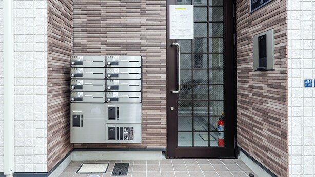 A building entrance with a brown door, a fire extinguisher, and a row of mailboxes. - Zenith Shinjuku Hinoki Building A (Tokyo)