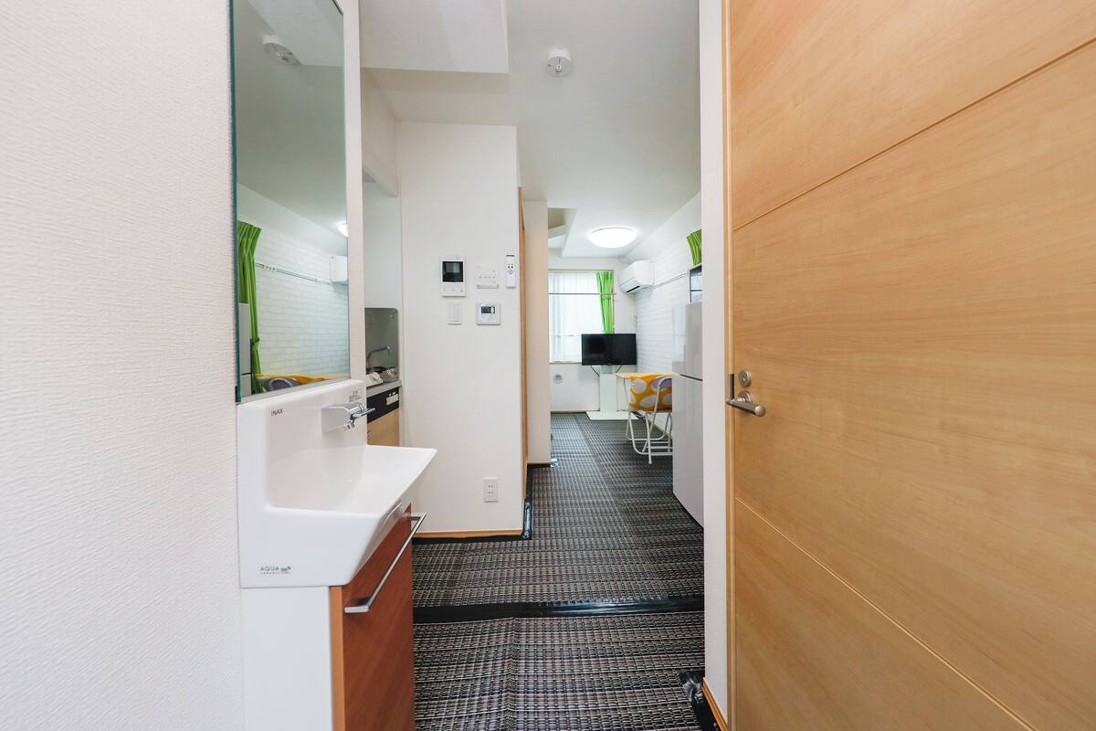 A narrow hallway with a white sink, a mirror, and a wooden door.